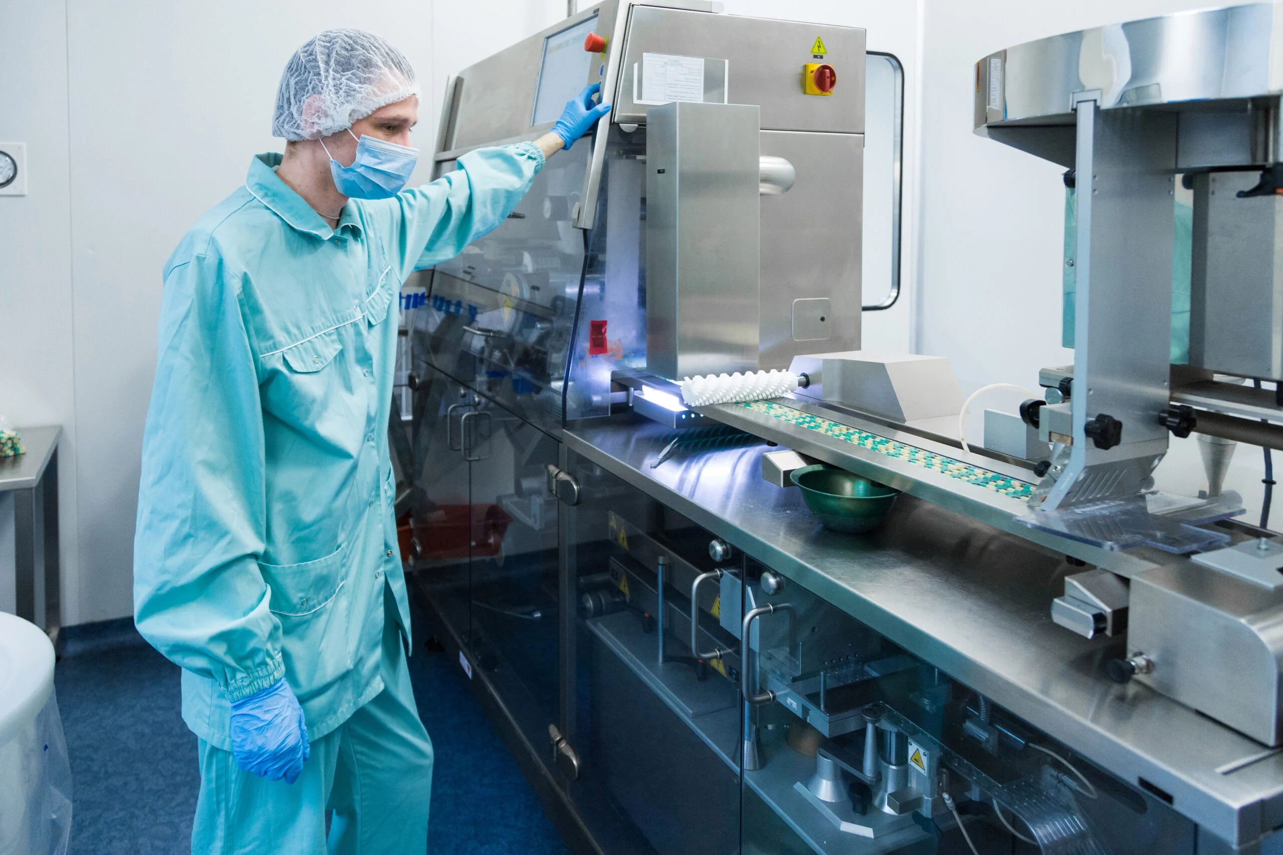 Pharmaceutical industry man worker in protective clothing operating production of tablets in sterile working conditions Worker in protective clothing operating pharmaceutical production equipment